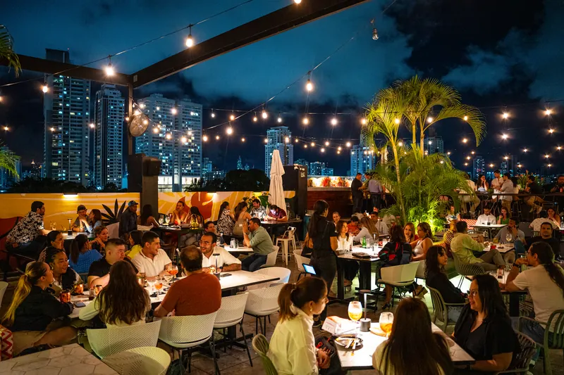 Rooftop Terrat de noche con palmas, luces y la ciudad de Panamá de fondo